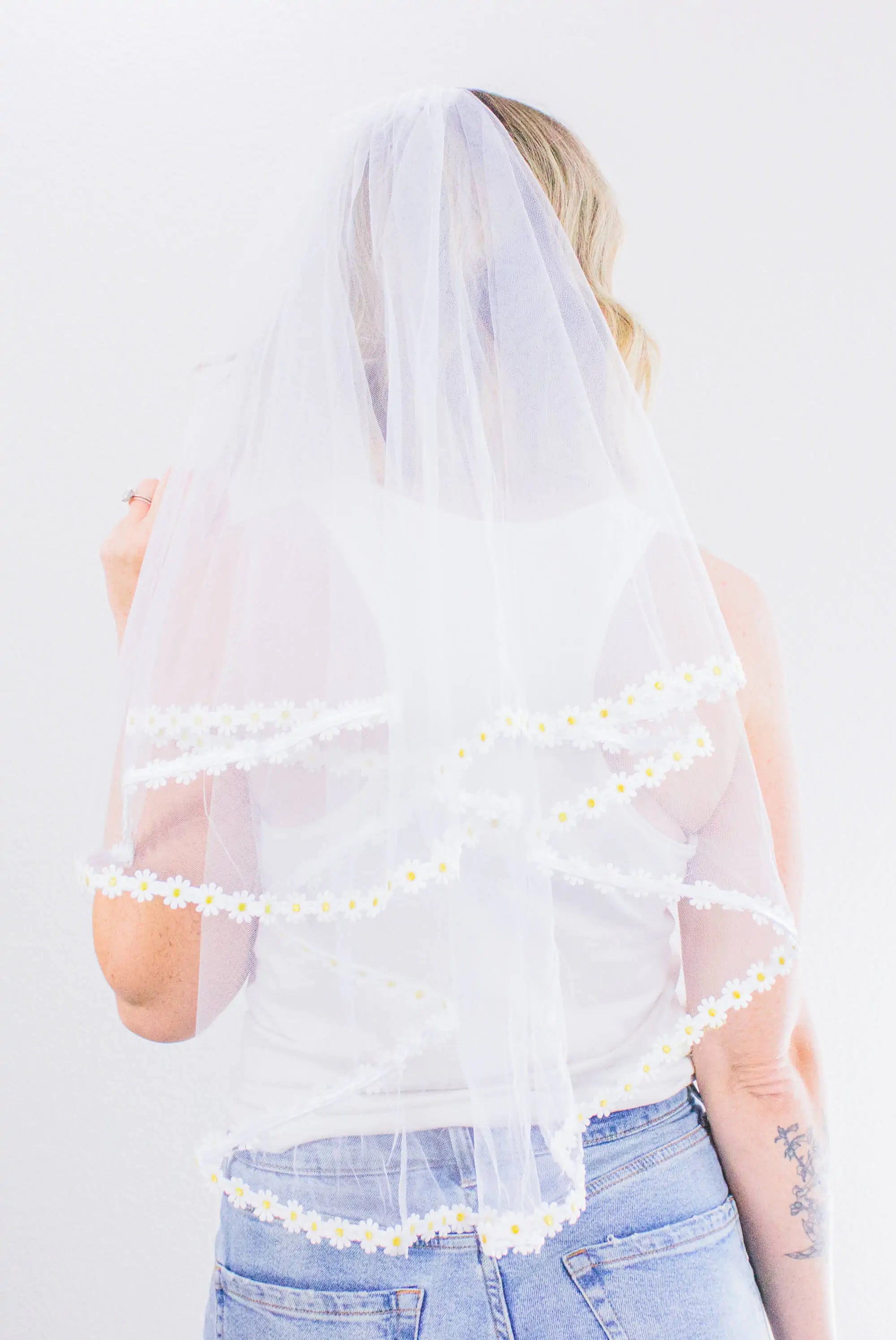 Person wearing a white veil with floral trim on a plain background