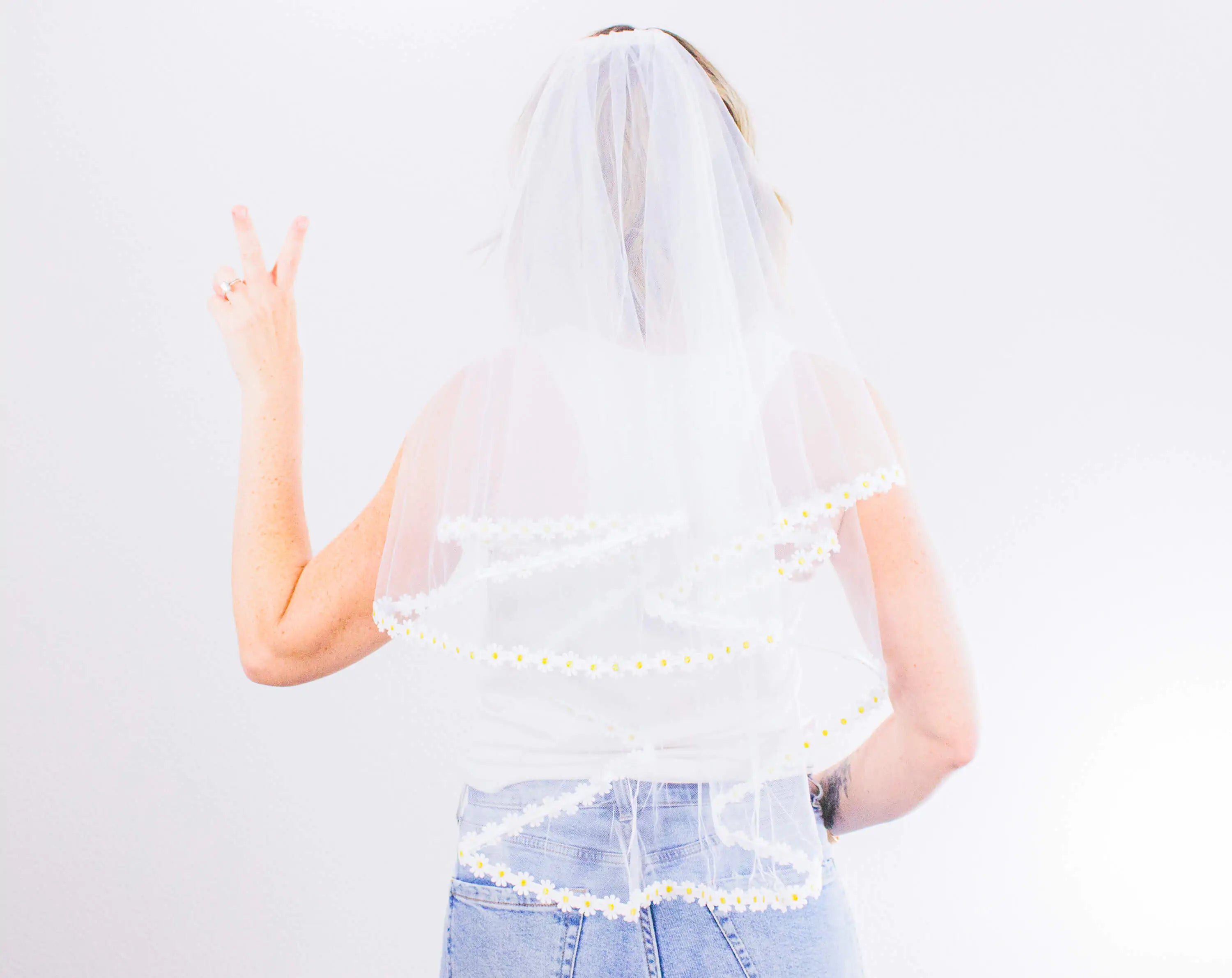 Person wearing a white lace veil and denim skirt on a light gray background