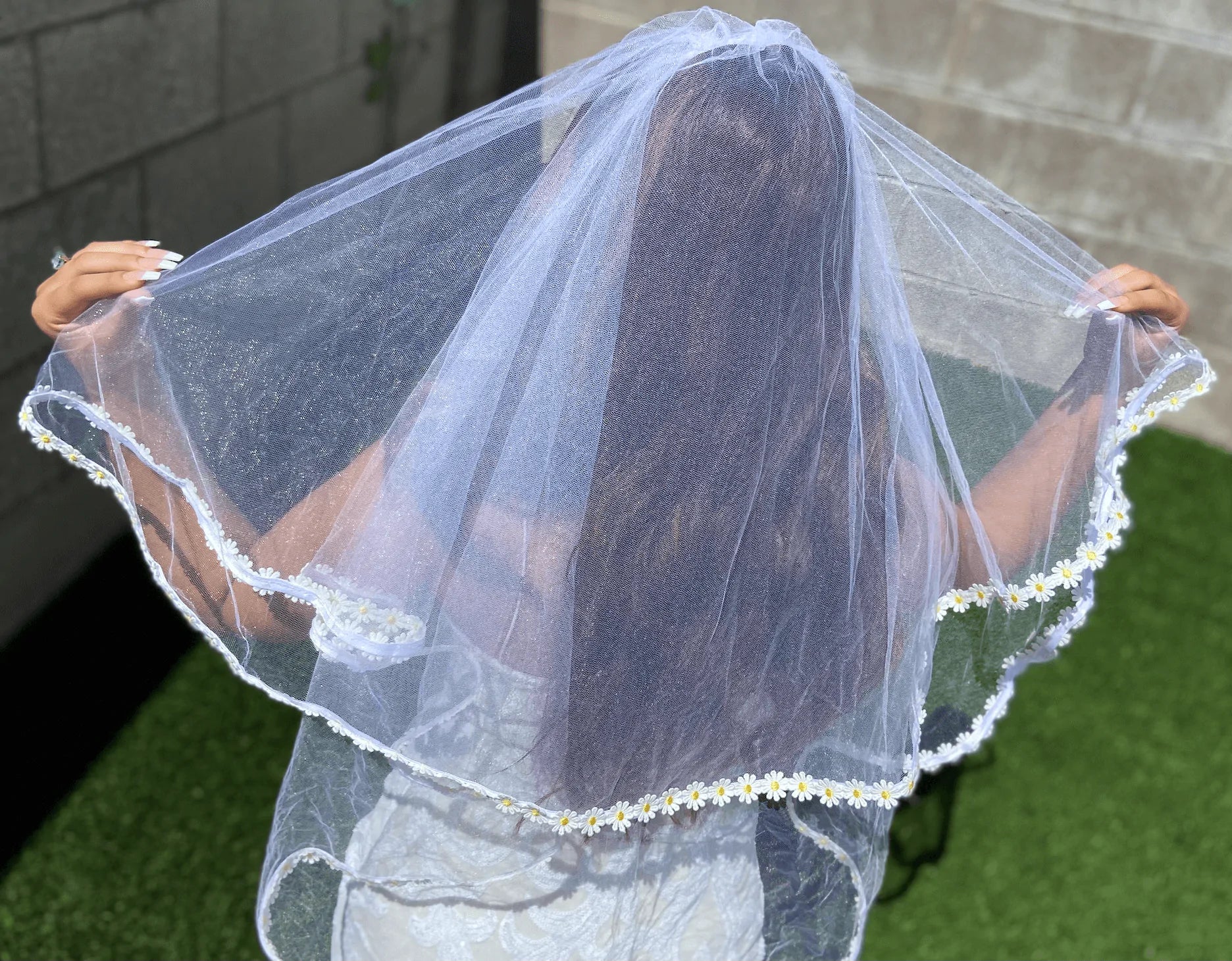 Person holding a white veil with floral trim outdoors.